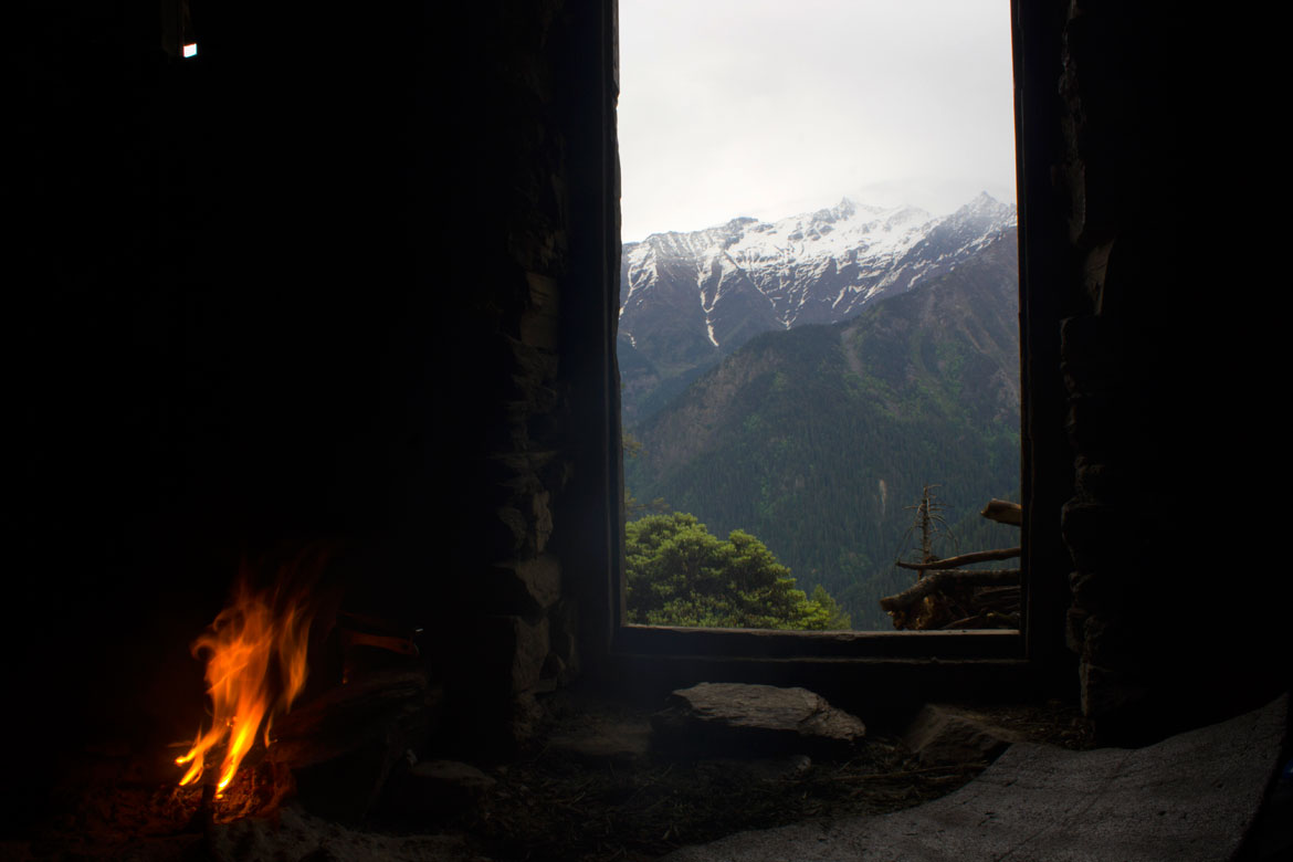 Snow-capped peaks as can be seen from the interiors of a hut on Shilt meadow. A fire burns inside as preparations for dinner get underway