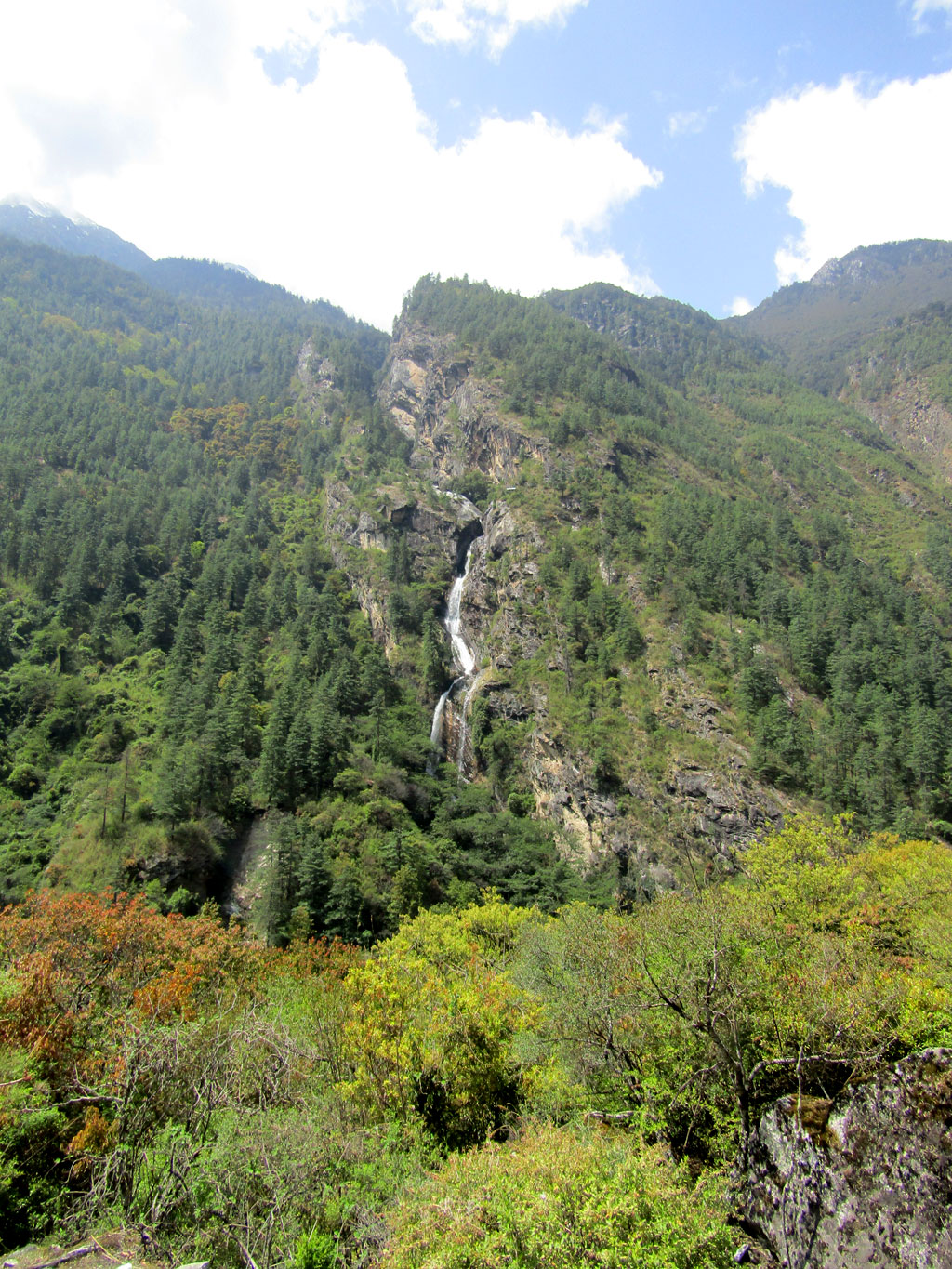 A waterfall cascades down through a forest above the village of Bihi, deep inside the Manaslu Conservation Area