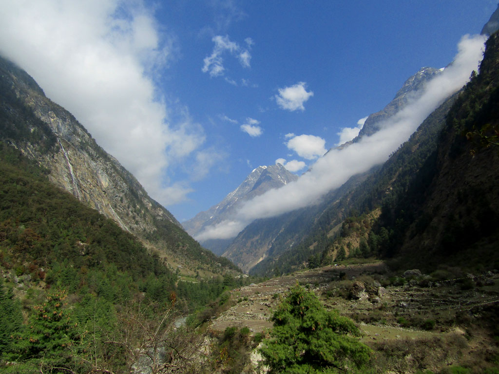 Cloud banners drape the Budhi Gandaki valley, beyond the village of Namrung. As the trail enters the high country, spectacular granite pinnacles appear, while fields of barley add colour to the rugged scene