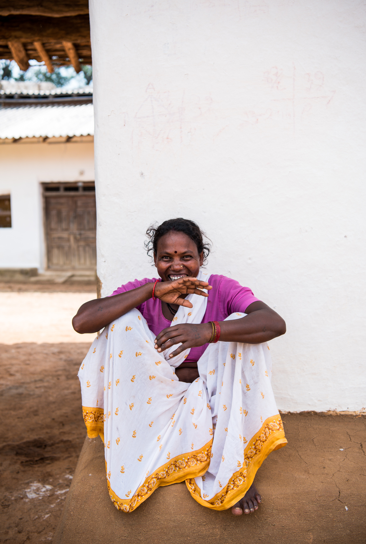 A Gond woman sits outside her mud home. 