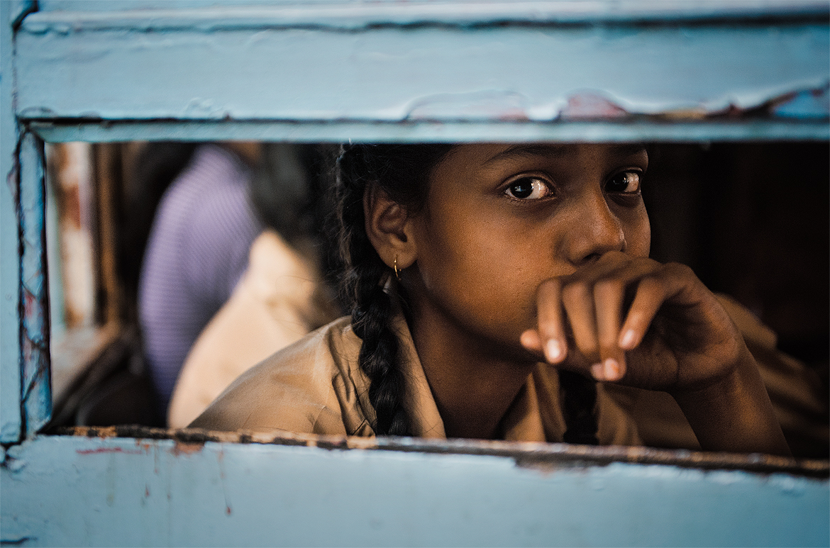 A young girl gazes into the camera through the tram's window